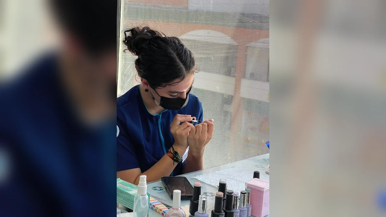 Profesional con tapabocas y uniforme azul realizando manicura profesional a clienta con instrumental técnico especializado