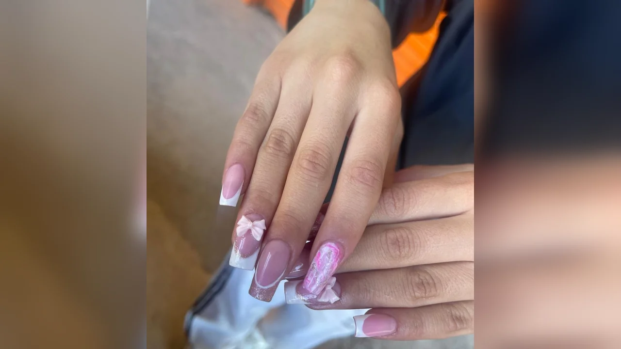 Uñas acrílicas con diseño francés decoradas con lazos rosas y detalles de glitter brillante